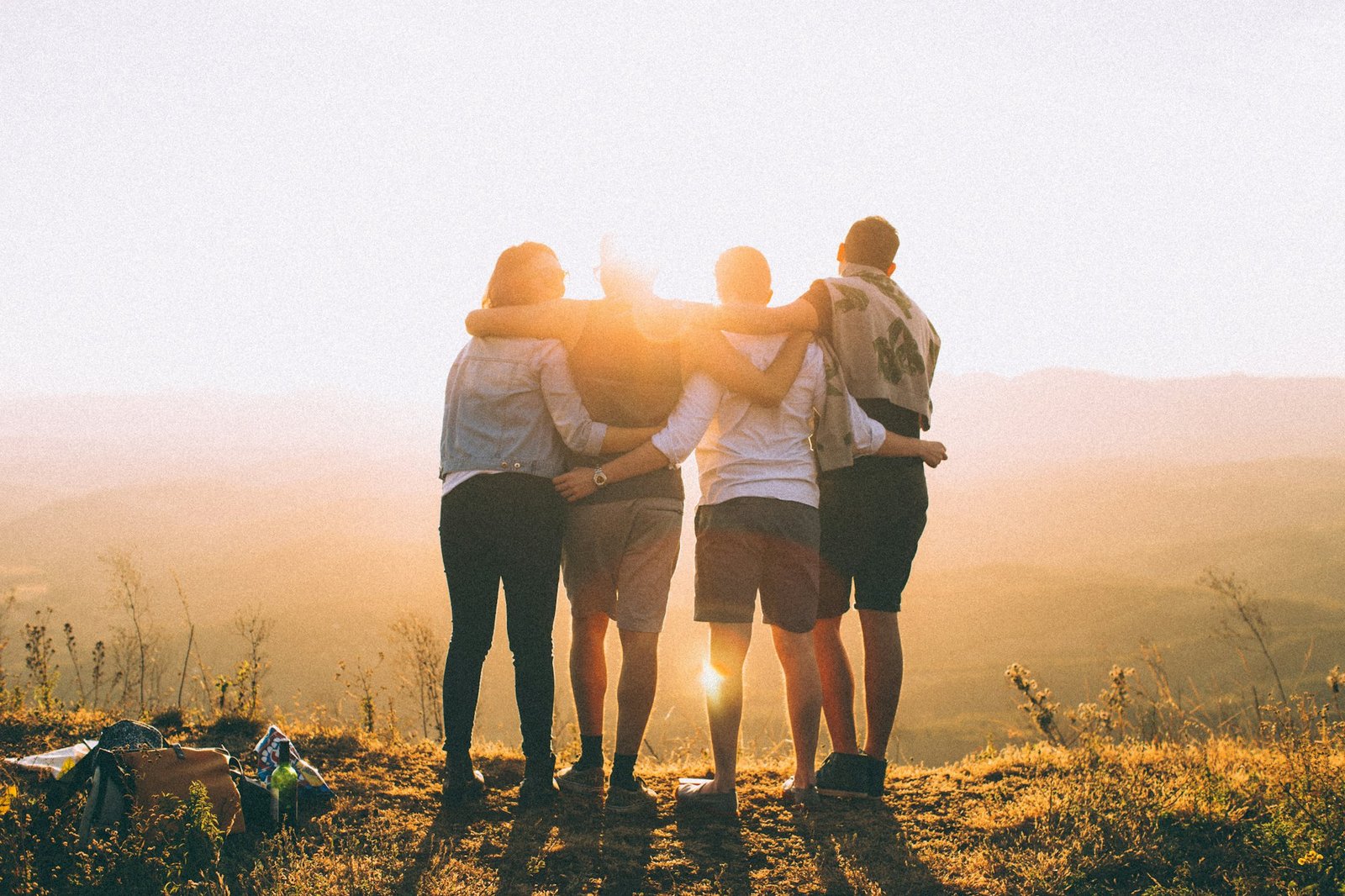 Four friends with their arms around each other, watching the sunset